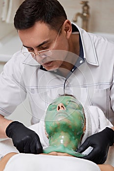 male beautician removing green alginate mask from face of woman