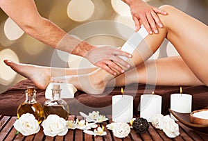 Male beautician waxing woman's leg in spa photo