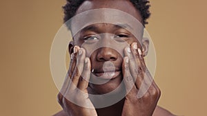 Male beauty care. Close up of young african american man applying moisturizing cream on his cheeks, pampering face skin