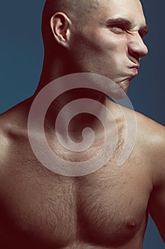 Male beauty concept. Handsome male model with earring posing over blue background. Perfect skin, shaved head, hairy muscular body