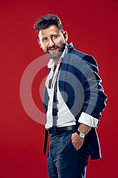 Male beauty concept. Portrait of a fashionable young man with stylish haircut wearing trendy suit posing over red