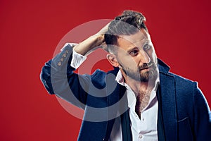 Male beauty concept. Portrait of a fashionable young man with stylish haircut wearing trendy suit posing over red