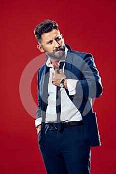 Male beauty concept. Portrait of a fashionable young man with stylish haircut wearing trendy suit posing over red