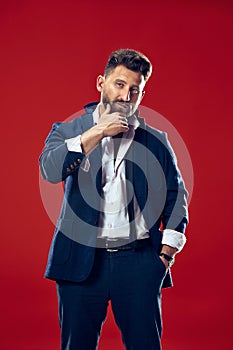 Male beauty concept. Portrait of a fashionable young man with stylish haircut wearing trendy suit posing over red