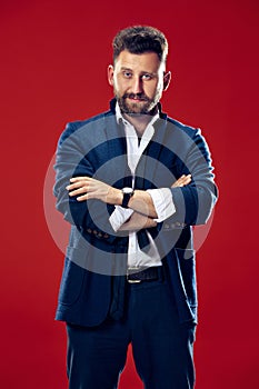 Male beauty concept. Portrait of a fashionable young man with stylish haircut wearing trendy suit posing over red