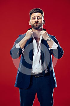 Male beauty concept. Portrait of a fashionable young man with stylish haircut wearing trendy suit posing over red