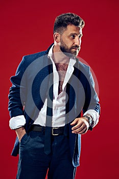 Male beauty concept. Portrait of a fashionable young man with stylish haircut wearing trendy suit posing over red