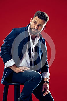 Male beauty concept. Portrait of a fashionable young man with stylish haircut wearing trendy suit posing over red