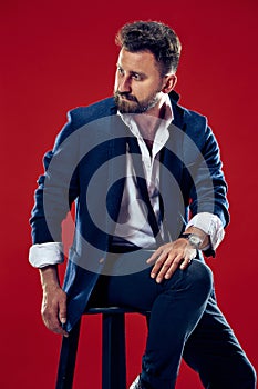 Male beauty concept. Portrait of a fashionable young man with stylish haircut wearing trendy suit posing over red