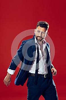 Male beauty concept. Portrait of a fashionable young man with stylish haircut wearing trendy suit posing over red