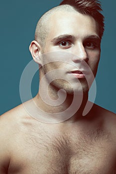Male beauty concept. Portrait of handsome muscular male model posing over blue background. Half-shaved head and healthy clean skin
