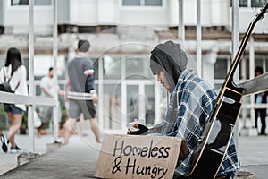 Male beggar in hood showing seeking human kindness sign on cardboard