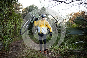 Male biker carrying mountain bike and walking on dirt track