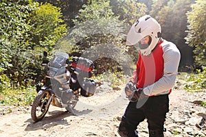 Male biker, motorcyclist in a white helmet. Stands next to a long-distance touring motorcycle. Side bags and luggage. mountain