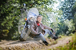 Male biker sitting on dirt road near motorcycle