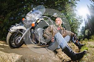 Male biker sitting on dirt road near motorcycle