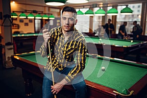 Male billiard player with cue poses at the table