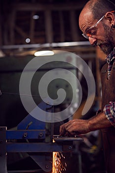 Male Blacksmith Shaping Metalwork On Belt Sander With Sparks photo