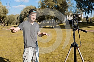 A male blogger is broadcasting video on a digital camera in a park. Remote freelance work, business coach, lifestyle