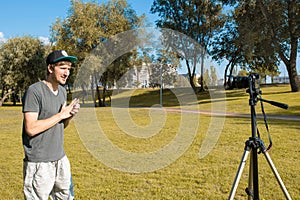 A male blogger in a park records a video tutorial on camera. blogging concept. Vlog, freelance work