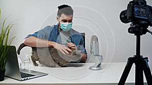 Male Blogger Streaming Wearing Medical Mask Playing with Cat. Video Content Maker. Virus Concept Video. Blogger Medical