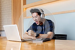 Male blogger watching video in social networks via headphones while updating software on laptop computer, Asian man listening audi