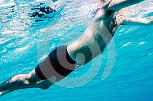 A male body underwater swimming in a clear blue sea and the face