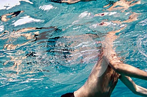 A male body underwater swimming in a clear blue sea and the face