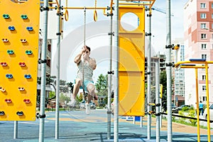 male bodybuilder athlete, trains on a street sports field. pull-up on a rope