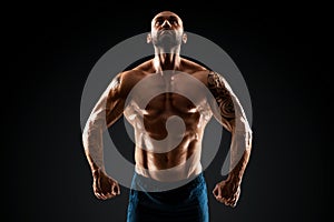 Male bodybuilder with light stubble and bare torso shows muscularity against a dark background. The concept of a fitness club,