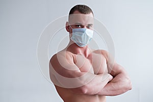 A male bodybuilder in a medical mask crossed his arms over his muscular bare chest. The guy goes in for sports in