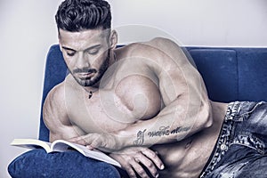 Male bodybuilder reading book on sofa