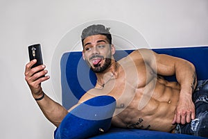 Male bodybuilder taking selfie photo on sofa