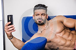 Male bodybuilder taking selfie photo on sofa