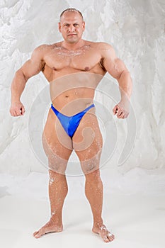 Male bodybuilder in trunks with snow on body shows