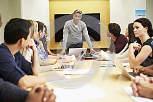 Male Boss Addressing Meeting Around Boardroom Table