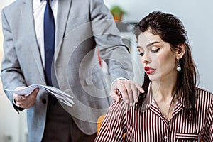 Male boss in grey costume deliberately touching female colleague