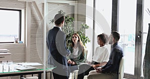 Male boss instructing mixed race interns at briefing meeting indoors.