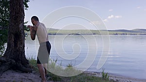Male boxer practicing on nature near tree. Boxer practicing on the lake. Boxer doing shadow Boxing in the nature near