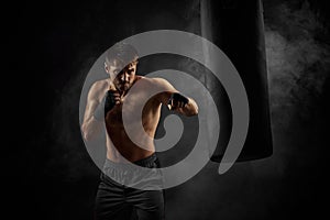 Male boxer punching in boxing bag on black background