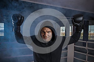 Male boxer in a sports ring raised two gloved hands above his head in a winning gesture