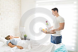 Male With Breakfast Tray Looking At Female Sleeping In Bed