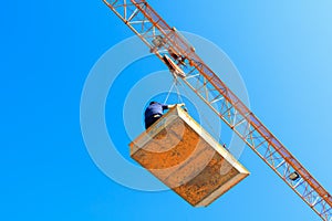 Male in bucket of Tower crane. building construction site. blue sky background