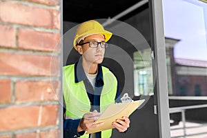 male builder with clipboard looking out window