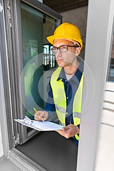 male builder with clipboard looking out window