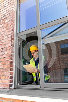male builder with clipboard looking out window