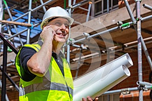 Male Builder Construction Worker on Building Site Using Cell Phone and Plans