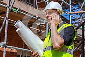 Male Builder Construction Worker on Building Site Using Phone and Plans