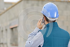 male builder foreman on building site using phone and plans