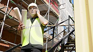 Male builder foreman construction worker on building site wearing a hardhat and talking on cell phone